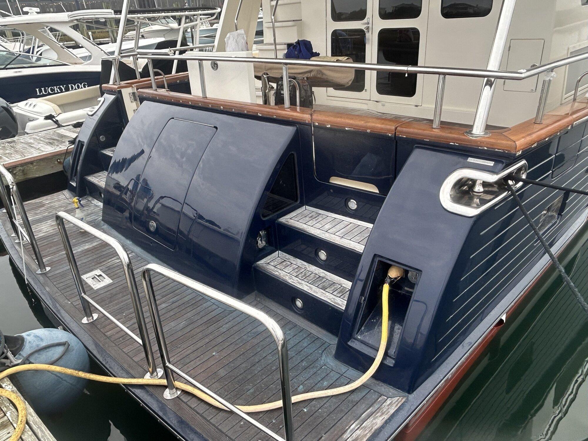 Finished boat with restored dark navy transom, teak steps, and polished stainless rails at a marina in Wrightsville Beach